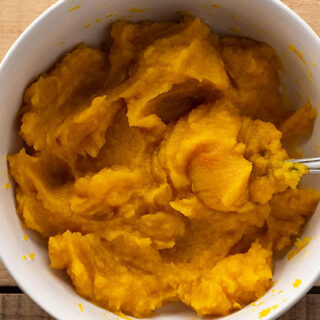 White bowl of homemade pumpkin puree on a wooden table.