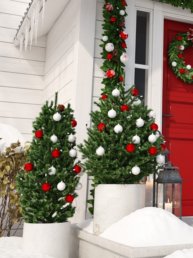 Two fake Christmas trees in containers on a porch.