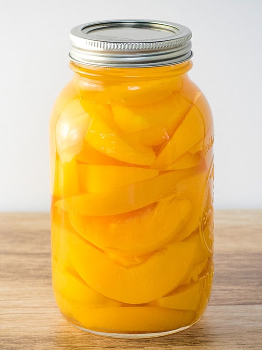 Jar of home canned peaches on a wooden table.