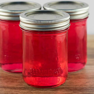 3 Jars of pink peony jelly on a table.