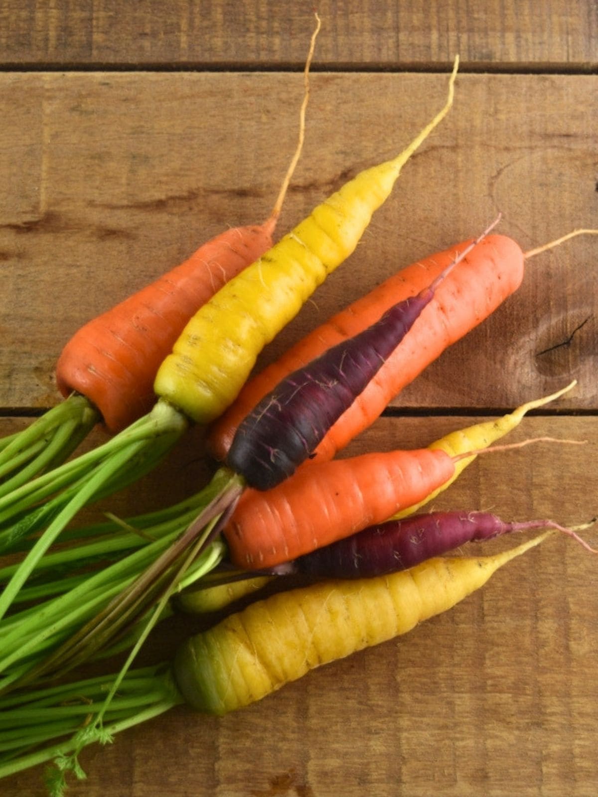 Rainbow blend carrots freshly picked from the garden set on a wooden table.