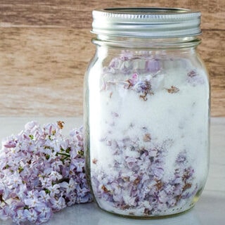 Lilac sugar in a mason jar with purple lilac flowers next to it on the table.