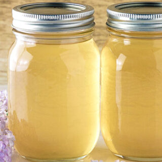 2 mason jars of lilac simple syrup on a table next to purple lilac flowers.