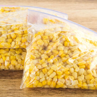 3 freezer bags of corn on a wooden table.