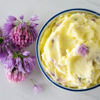 Homemade chive blossom butter in a serving bowl sitting next to fresh chive blossoms.
