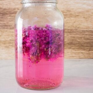 Canning jar of pink chive blossom vinegar sitting on a counter.