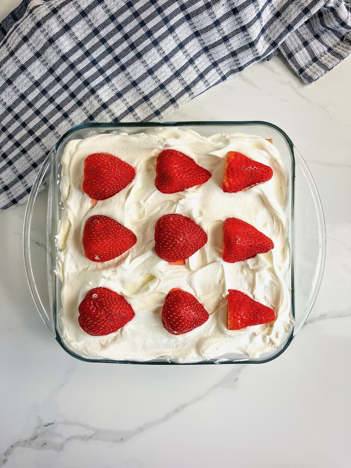 Strawberry icebox cake topped with halved strawberries in a 8x8 glass baking pan.