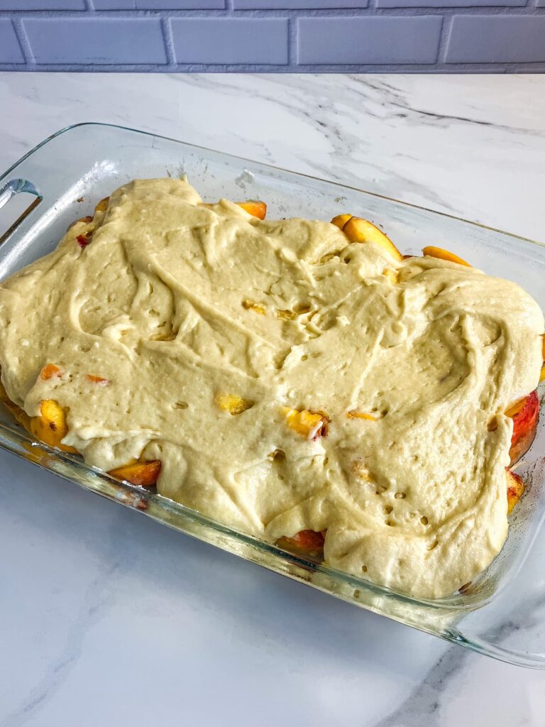 Peach cobbler topping spooned over the sliced peaches.