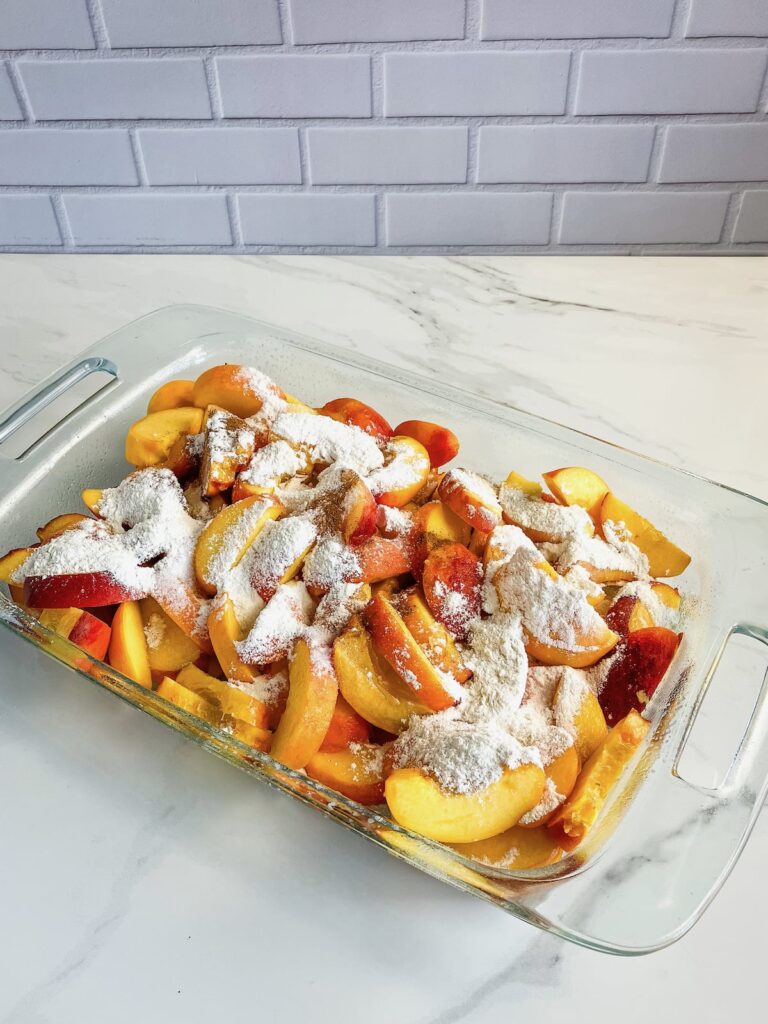 Flour mixture sprinkled on top of sliced peaches in a glass baking dish.