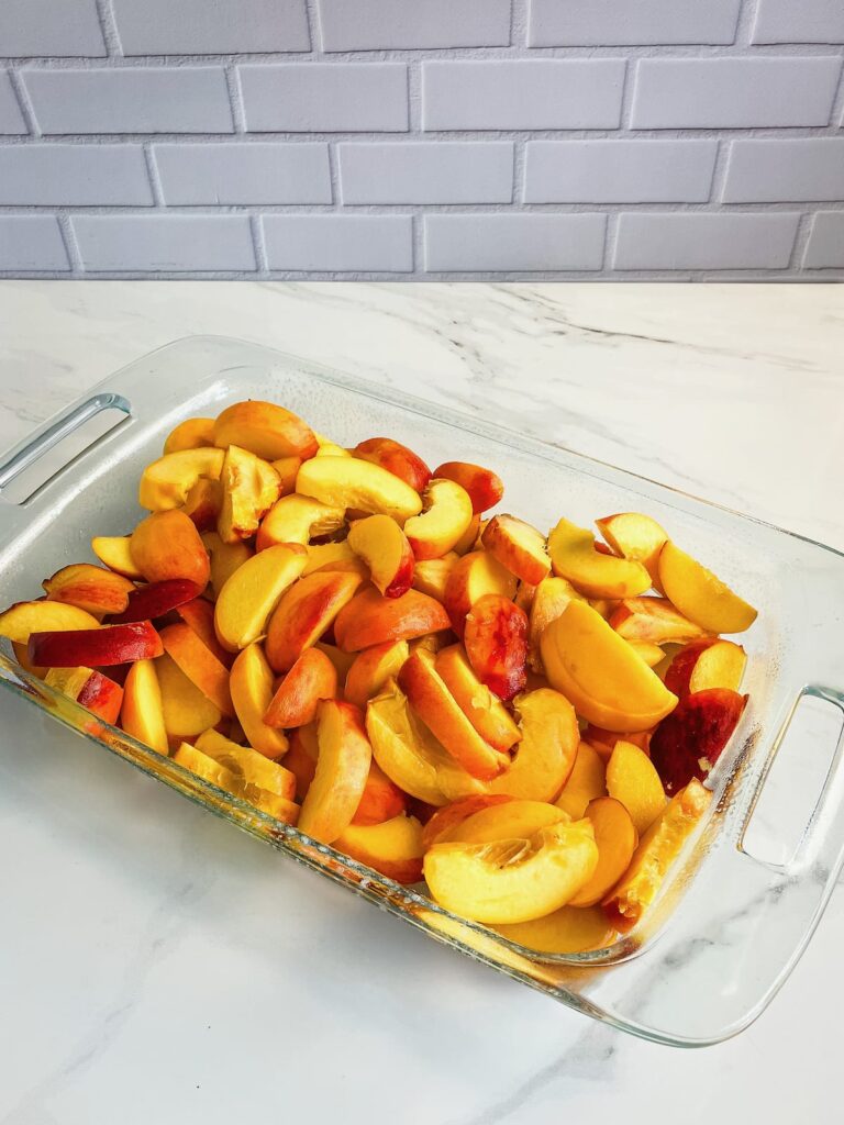 Glass baking dish filled with sliced peaches.