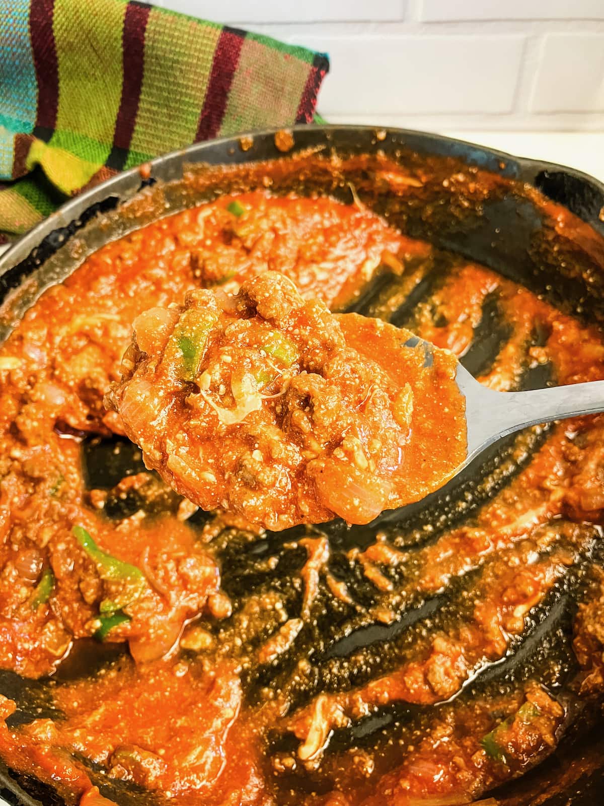 A large spoonful of meat sauce is held up over a skillet.