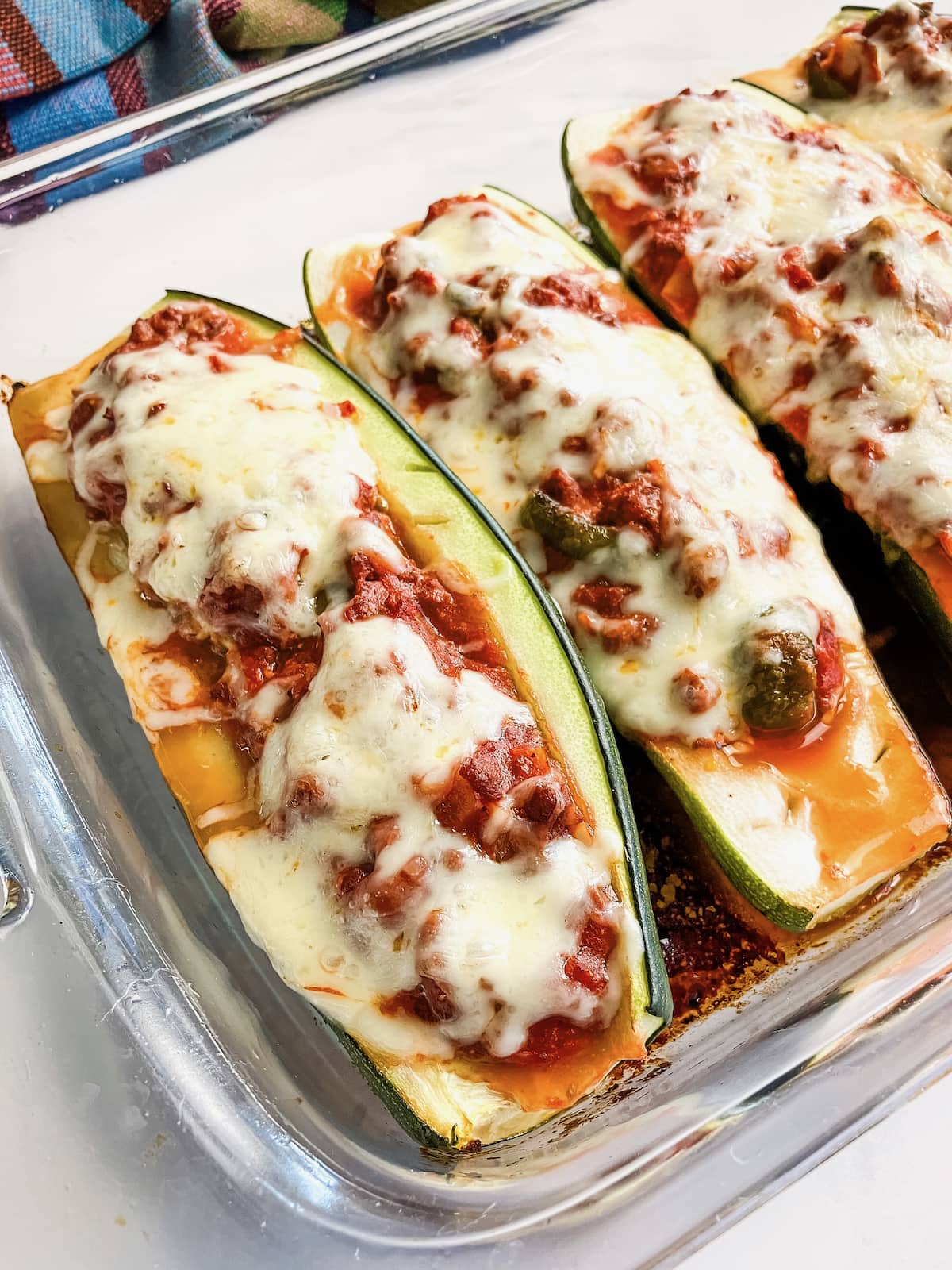 Stuffed zucchini filled with ground beef meat sauce and topped with cheese in a baking pan.