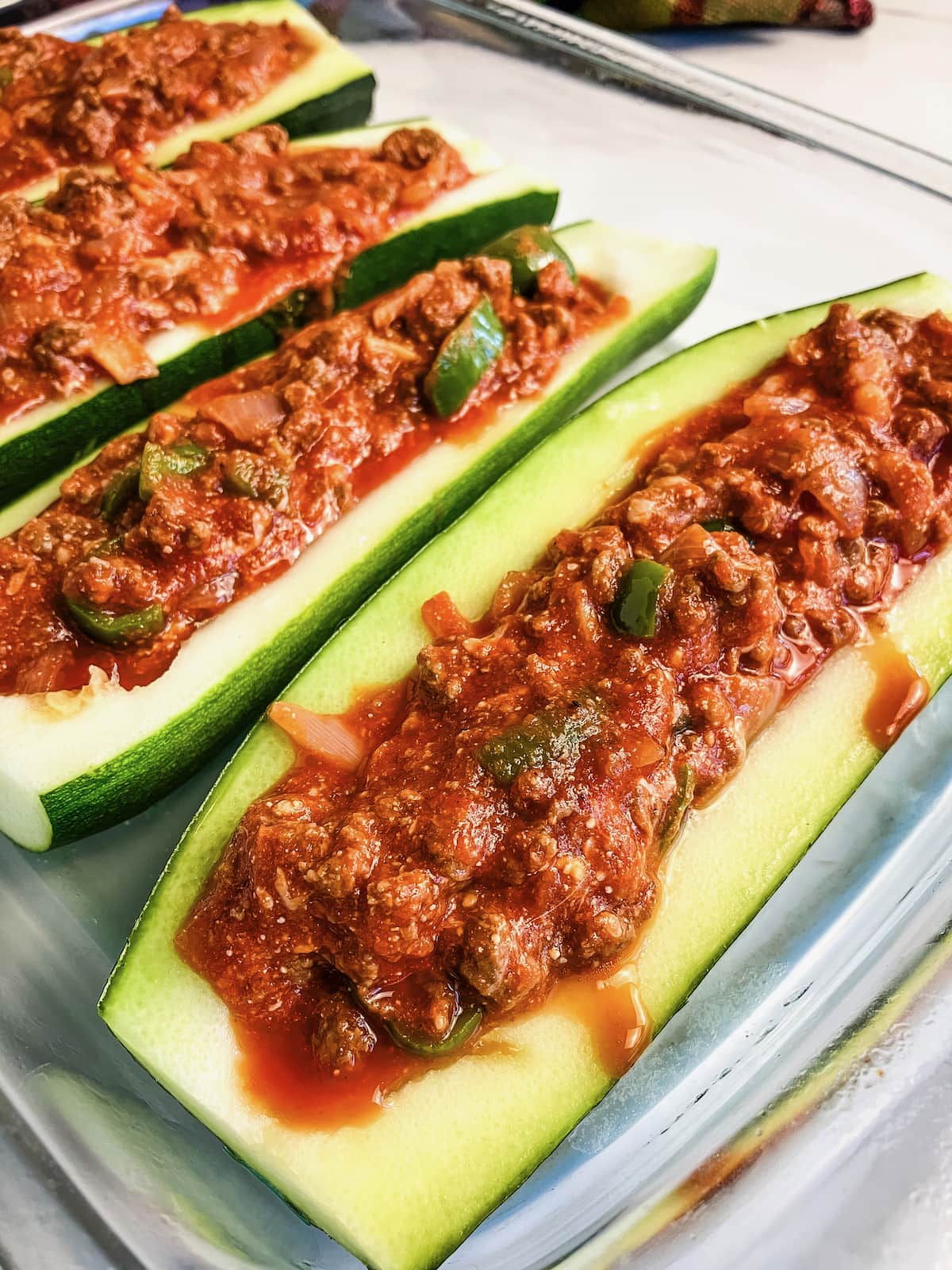 Zucchini stuffed with a meat sauce in a glass baking dish.