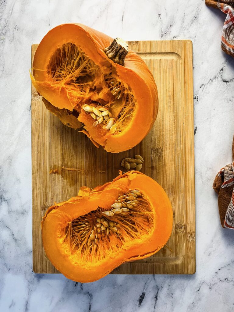A fully cooked pumpkin cut in half showing the seeds and pulp.