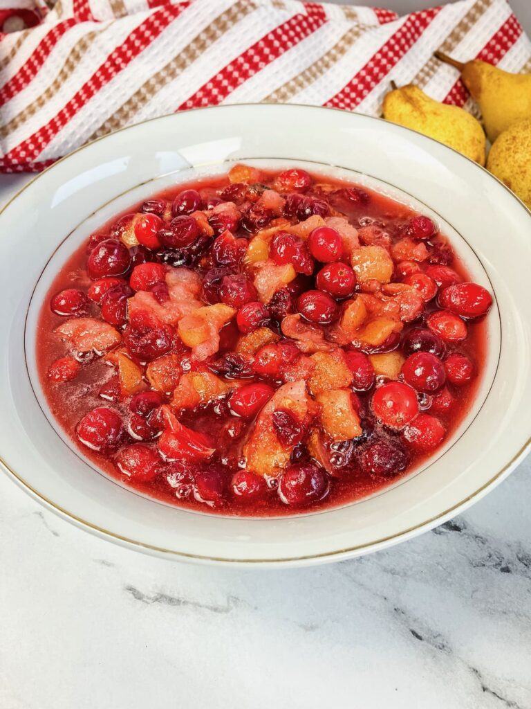White bowl filled with homemade cranberry pear sauce with fresh pears in the background.