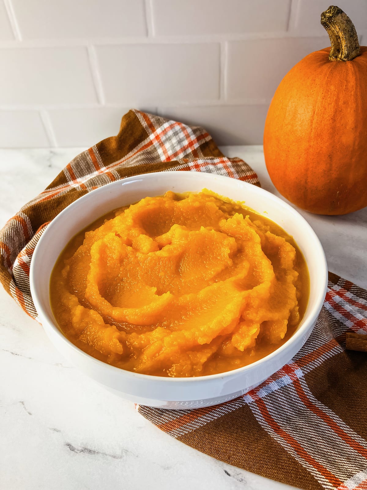 A white bowl filled with homemade pumpkin puree. In the background is a small pie pumpkin.