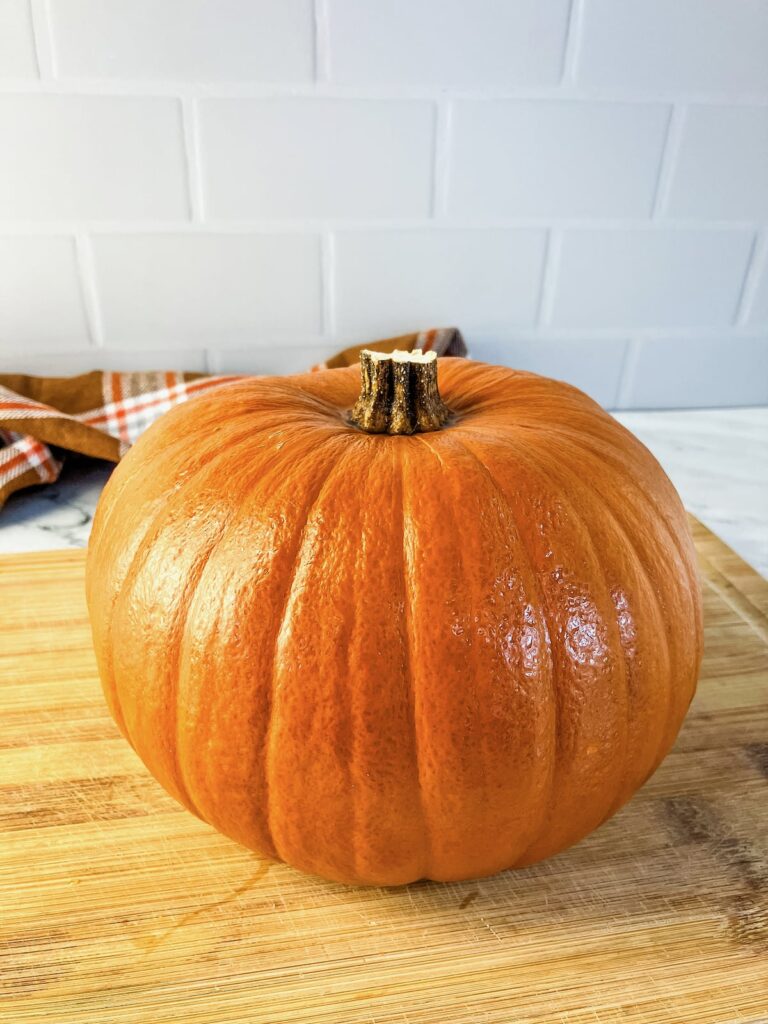 A cooked whole pumpkin on a wooden cutting board cooling.