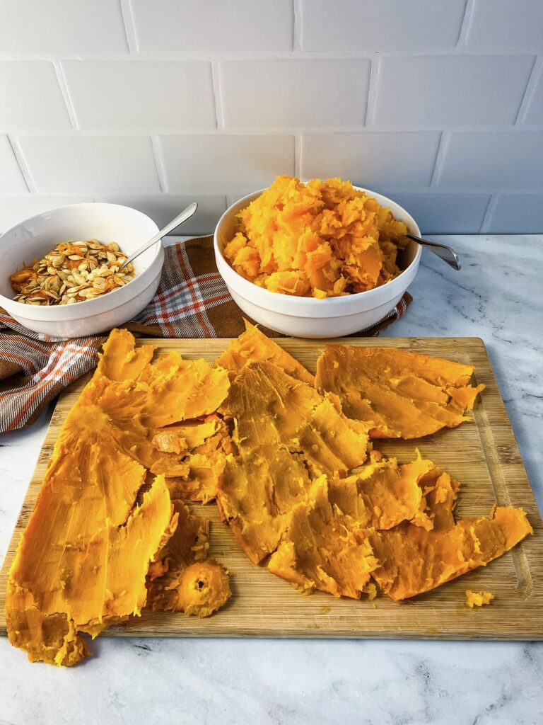 Pumpkin skin on a cutting board with bowls of pumpkin seeds and mashed pumpkin.