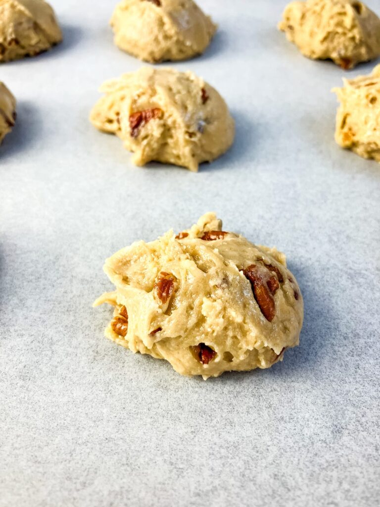 Butter pecan cookie balls on a parchment lined baking sheet.
