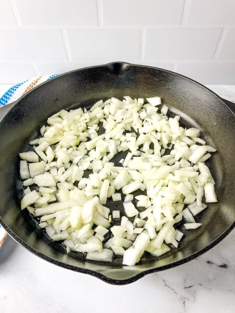 Cast iron skillet with diced onions cooking.