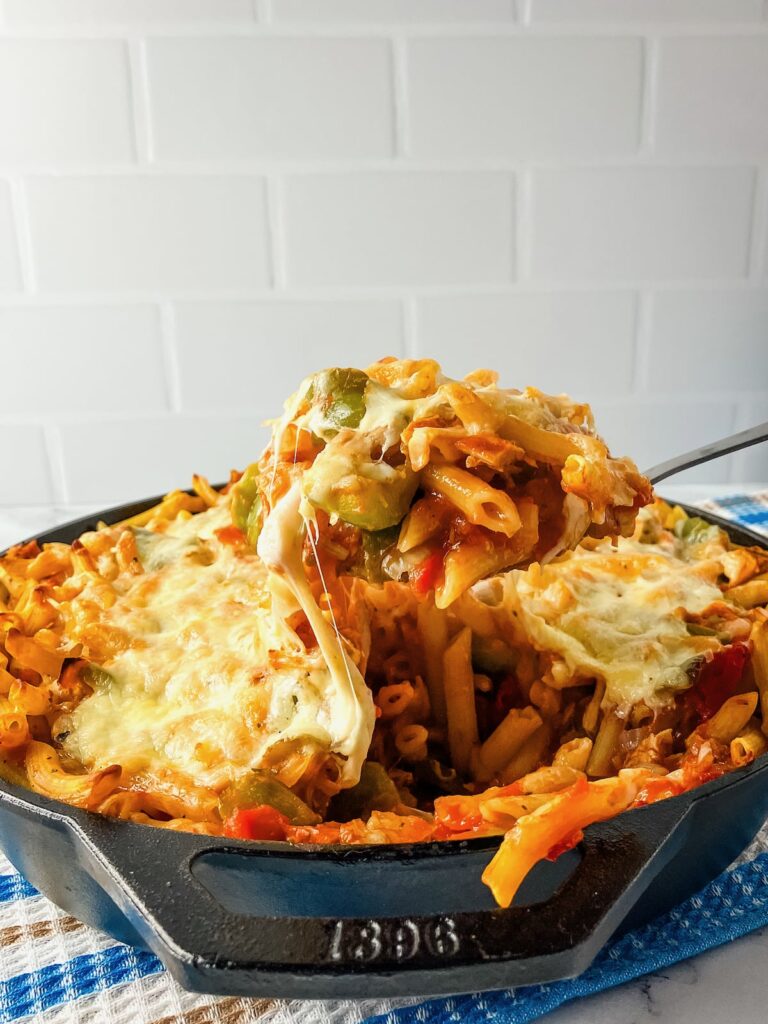 A serving spoon holding up a spoonful of turkey pasta bake over the pan.