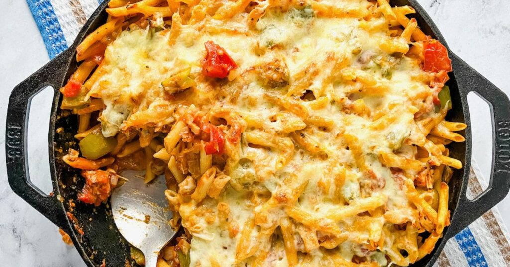 A cast iron skillet filled with leftover turkey pasta bake and a serving removed.