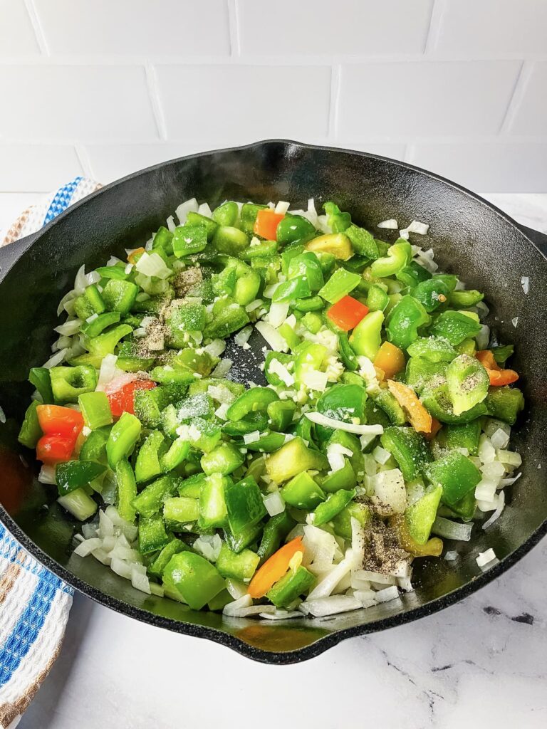 Skillet with onions, peppers, and garlic cooking.