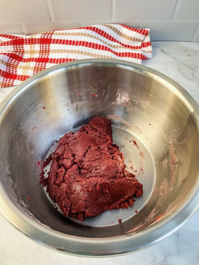 Red velvet cookie dough mixed together in a large stainless steel mixing bowl.