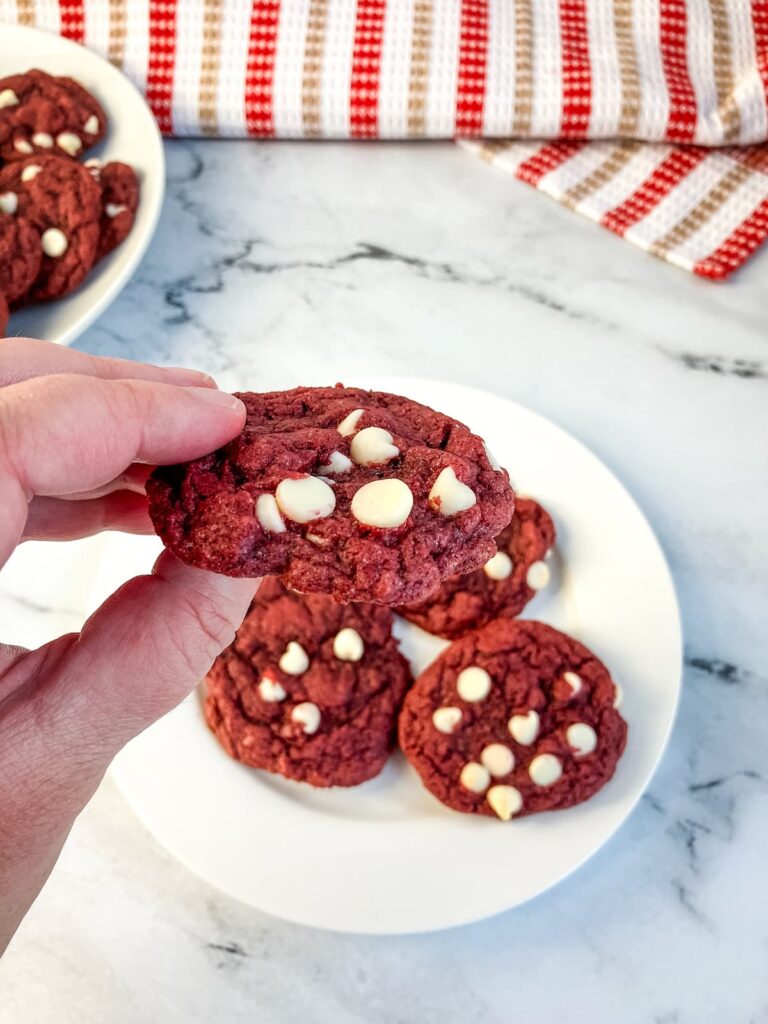 A hand holding up a cookie over a plate of cookies.