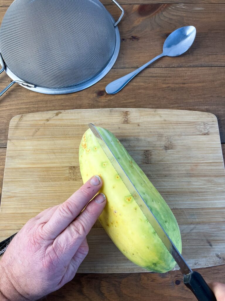 An over mature cucumber being cut in half on a wooden cutting board.