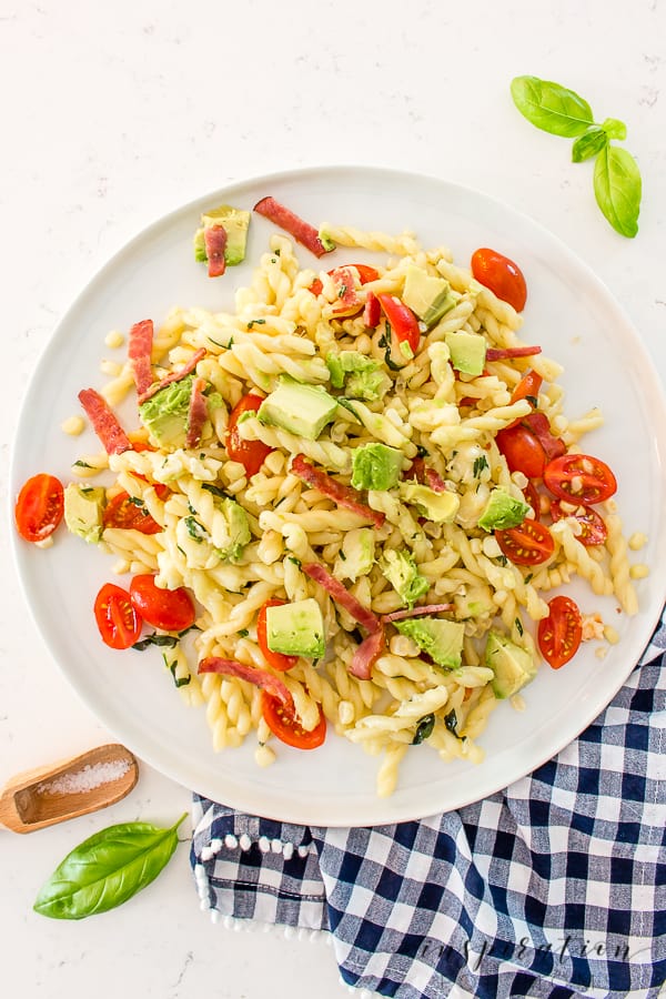 A plate filled with pasta salad with avocado, bacon, corn, and tomatoes.