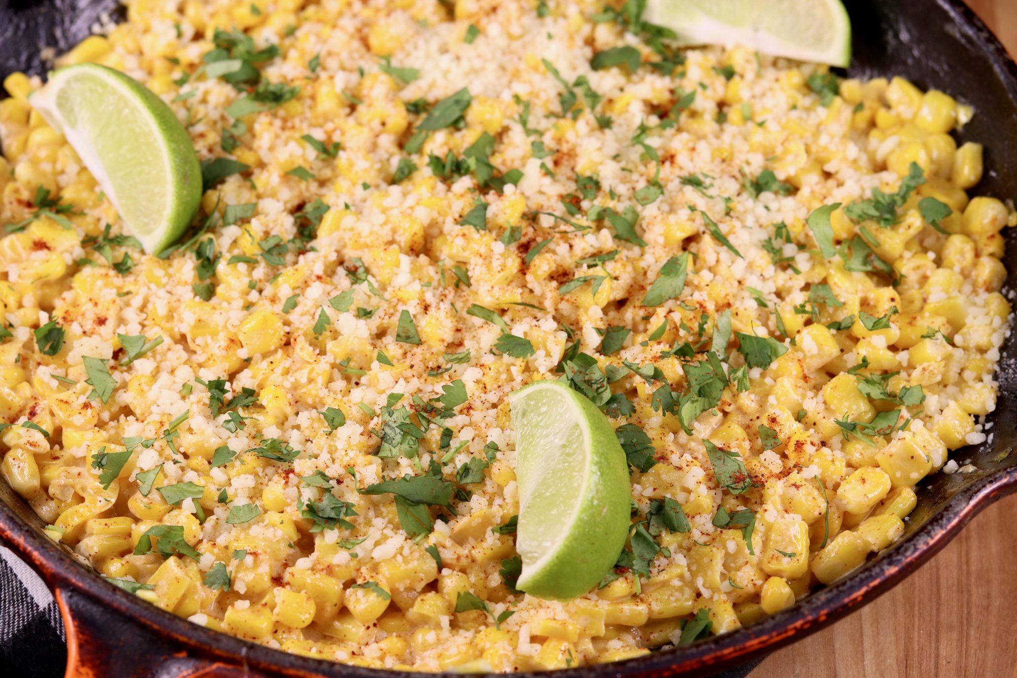 A skillet filled with Mexican street corn and topped with fresh limes.