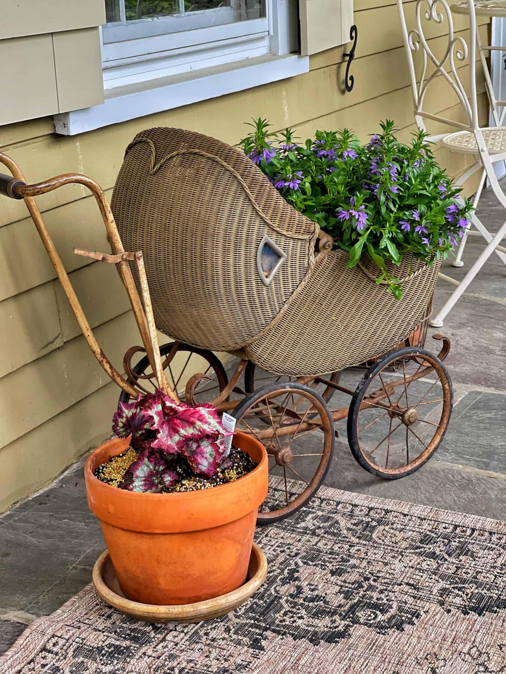 Vintage stroller turned into a flower planter on a porch.