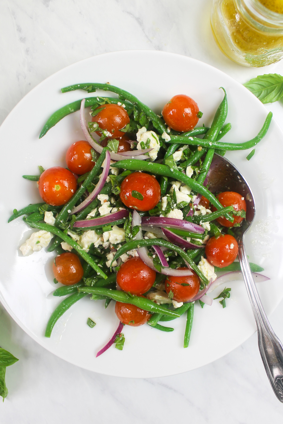 A white plate with homemade green bean salad with fresh cherry tomatoes and feta cheese.