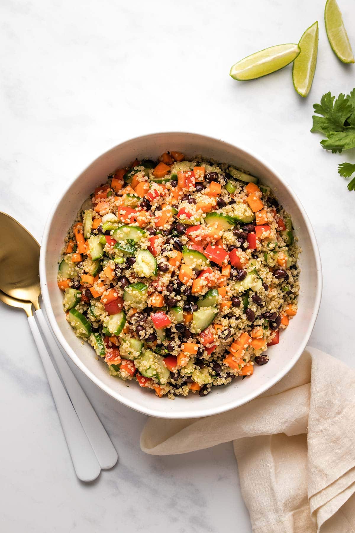 Quinoa black bean salad in a white serving bowl next to fresh limes.