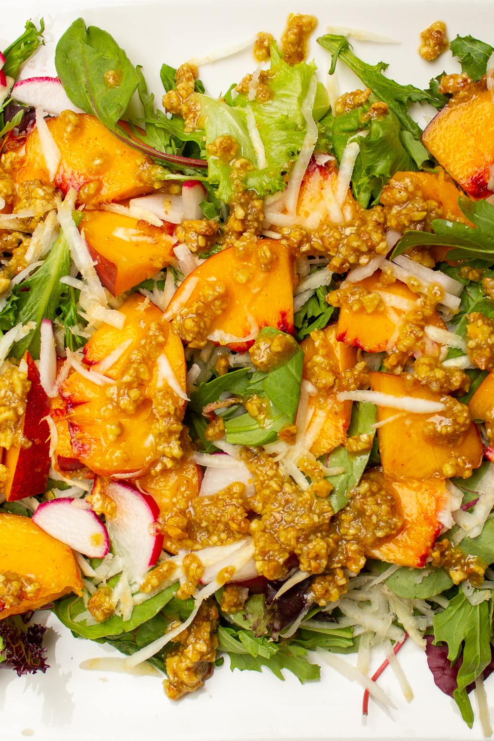 Arugula and peach salad with a walnut dressing on a white plate.