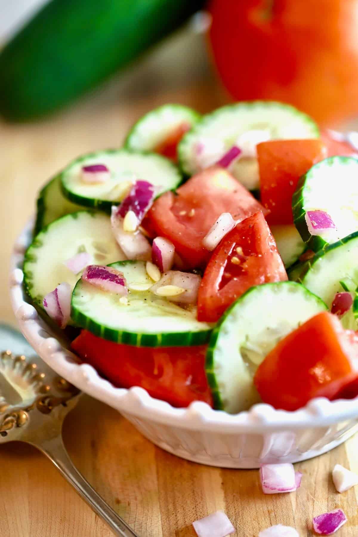 A pretty white bowl filled with cucumber and tomato salad.