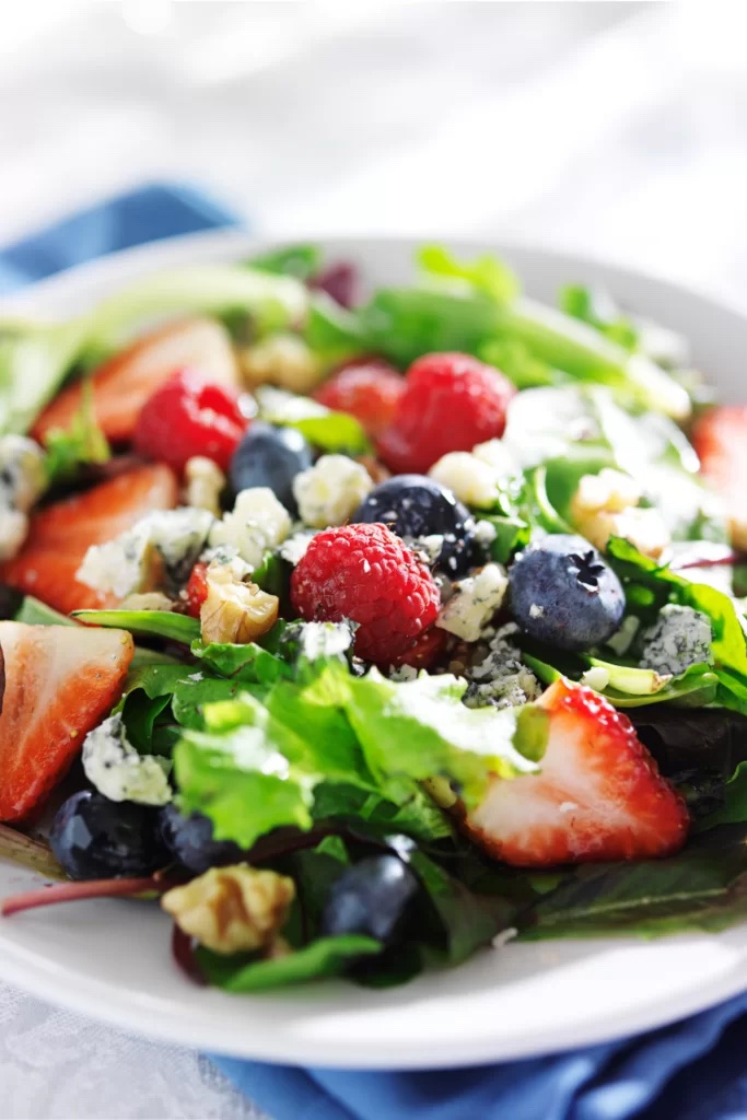 A homemade strawberry salad with walnuts and fruit on a white serving plate.