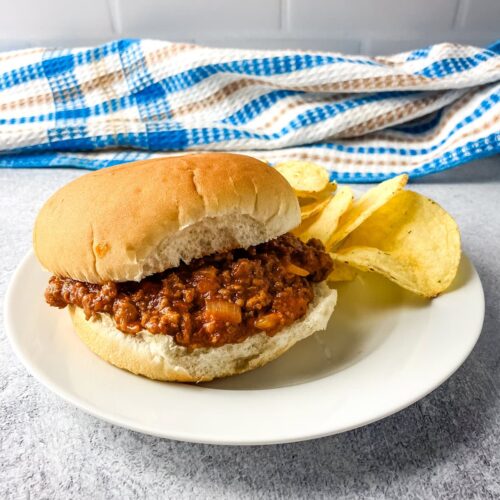 Homemade sloppy joes on a hamburger bun with chips on the side.