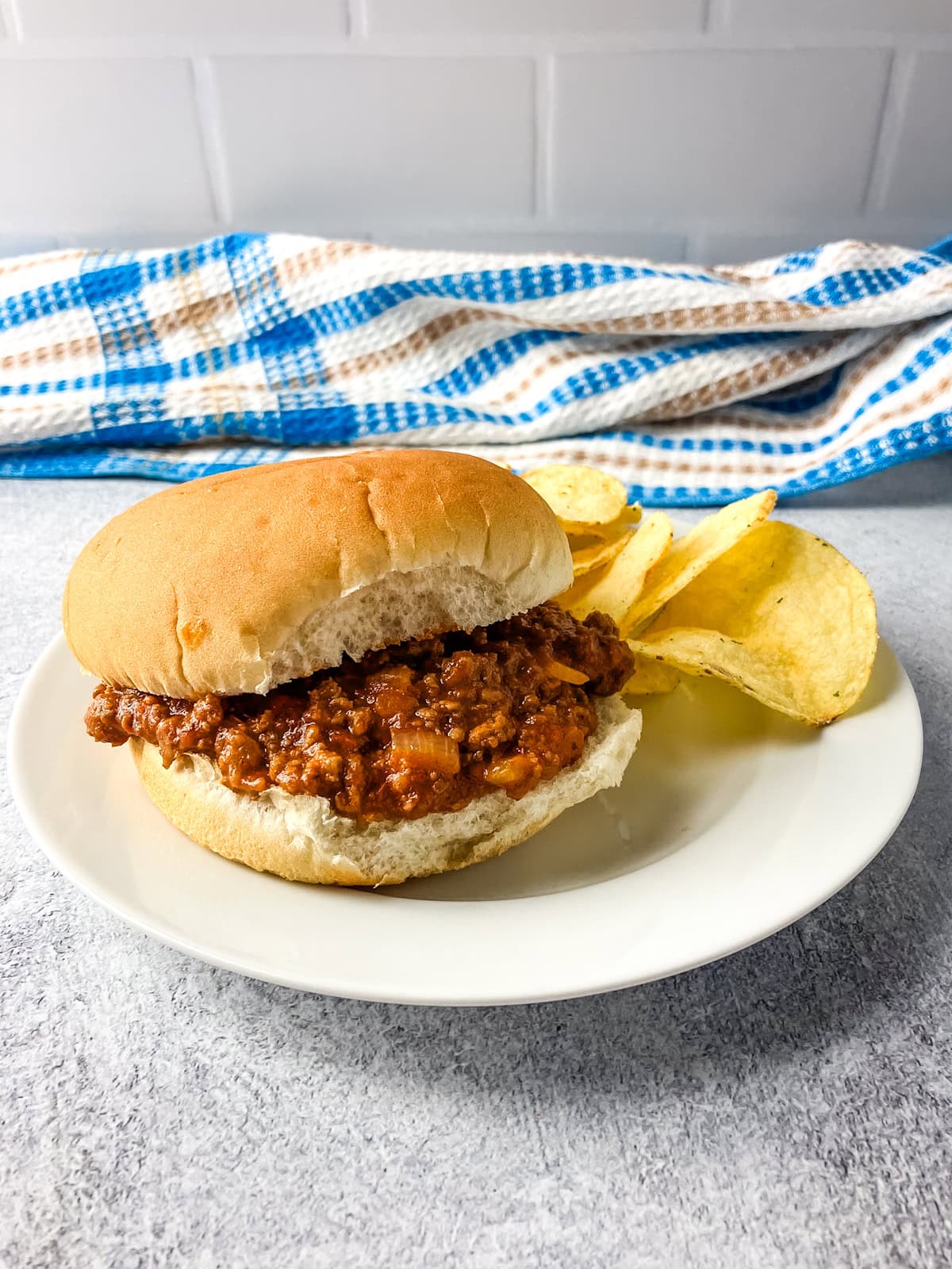 Homemade sloppy joes on a hamburger bun with chips on the side.