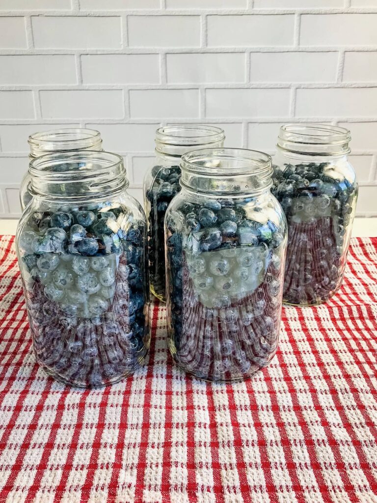 5 jars filled with blueberries on a red and white tea towel.