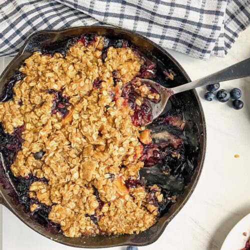 Blueberry peach crisp in a cast iron skillet with a serving spoon sitting in the pan.