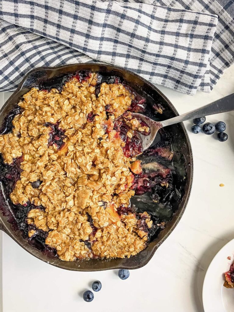 Blueberry peach crisp in a cast iron skillet with a serving spoon sitting in the pan.