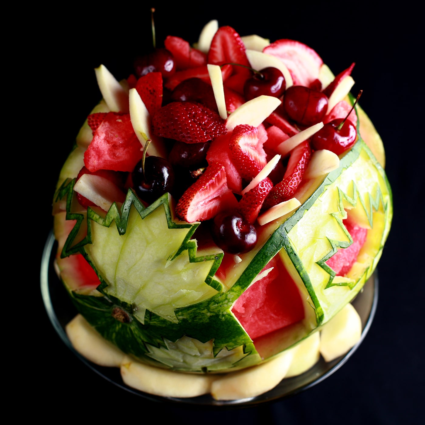Watermelon bowl carved with maple leaves for Canada Day and filled with red and white fruit.