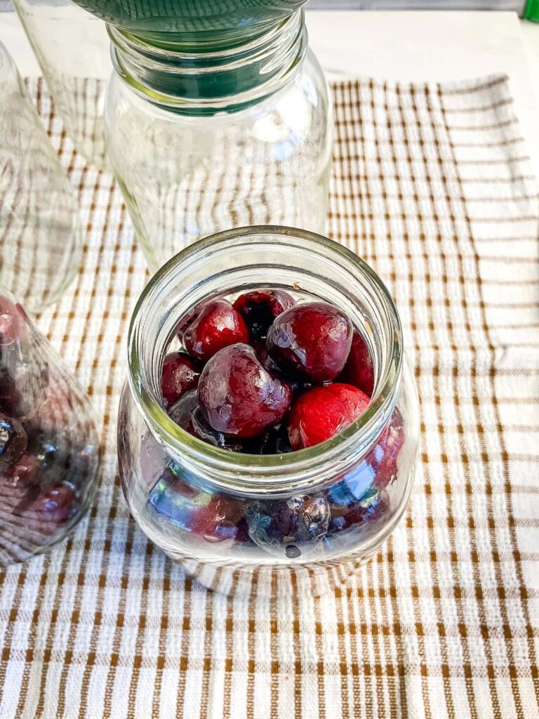 A mason jar filled with pitted cherries on a kitchen towel.