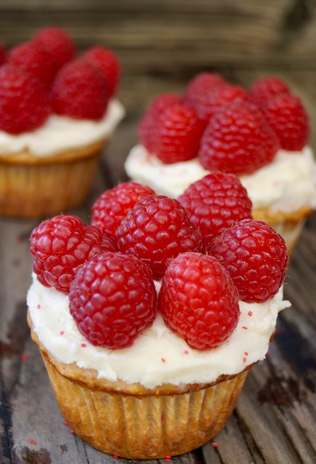 Homemade cupcake topped with icing and fresh raspberries.
