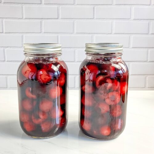 2 jars of home canned cherries on a counter.