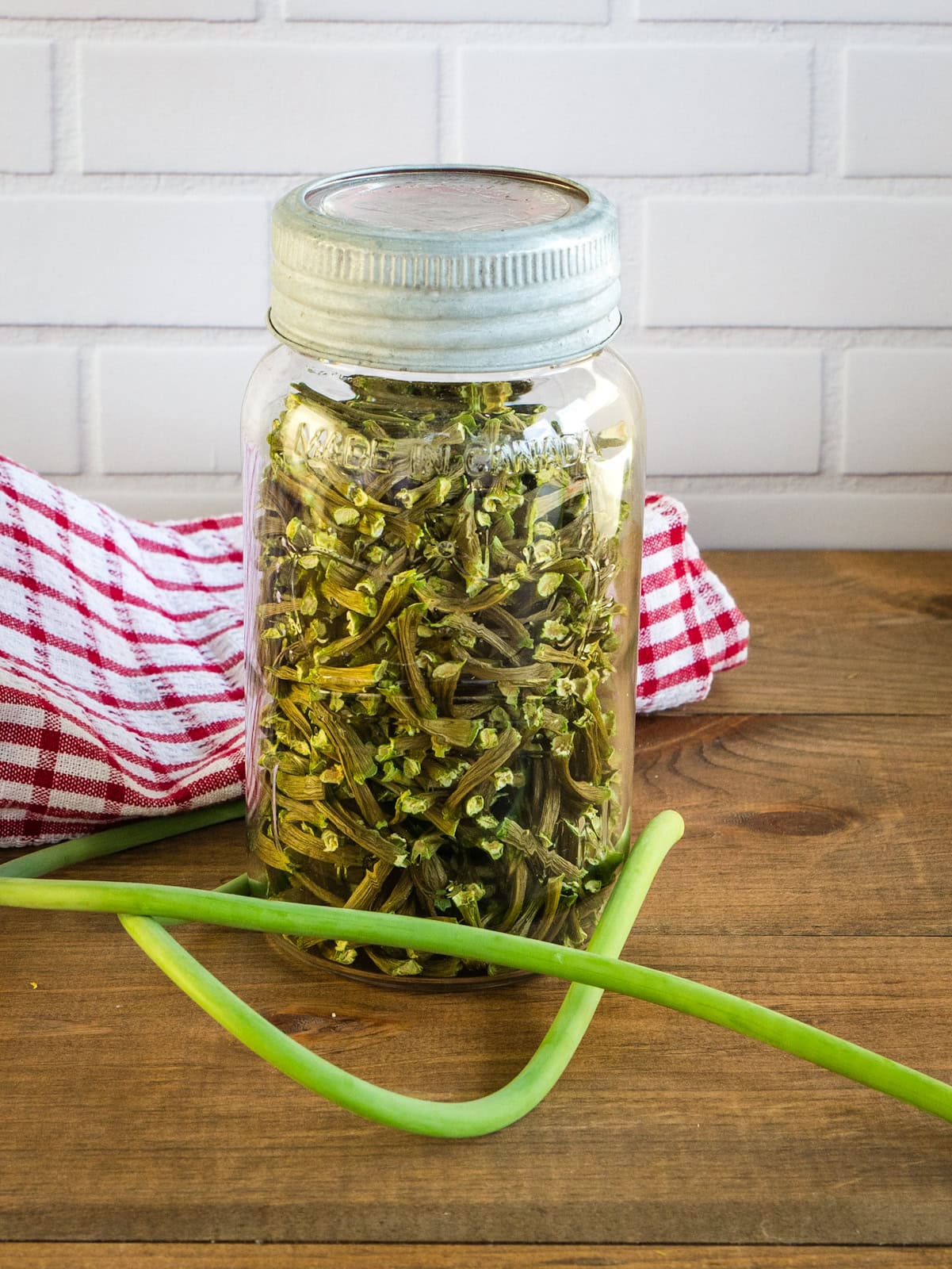 Vintage mason jar filled with dehydrated garlic scapes. Around the jar is a fresh garlic scape.