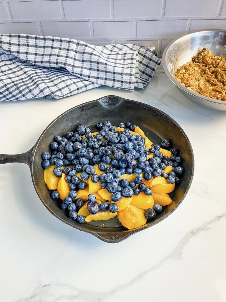 A cast iron skillet filled with fresh blueberries and peaches.
