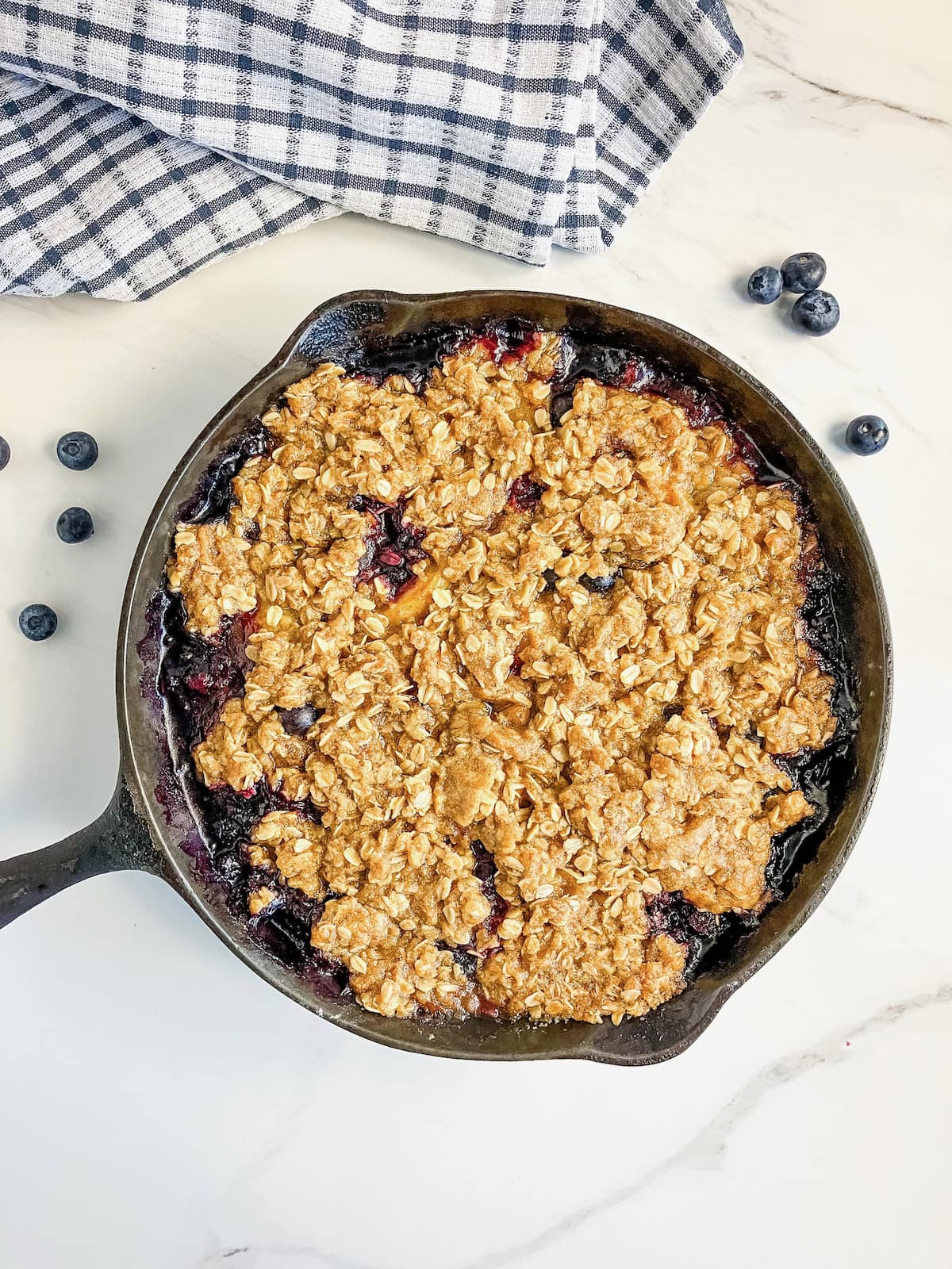 Warm blueberry peach crisp in a skillet with fresh blueberries on the counter around it.
